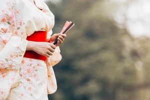 Asian girl wearing a kimono stand holding fan on a green grass